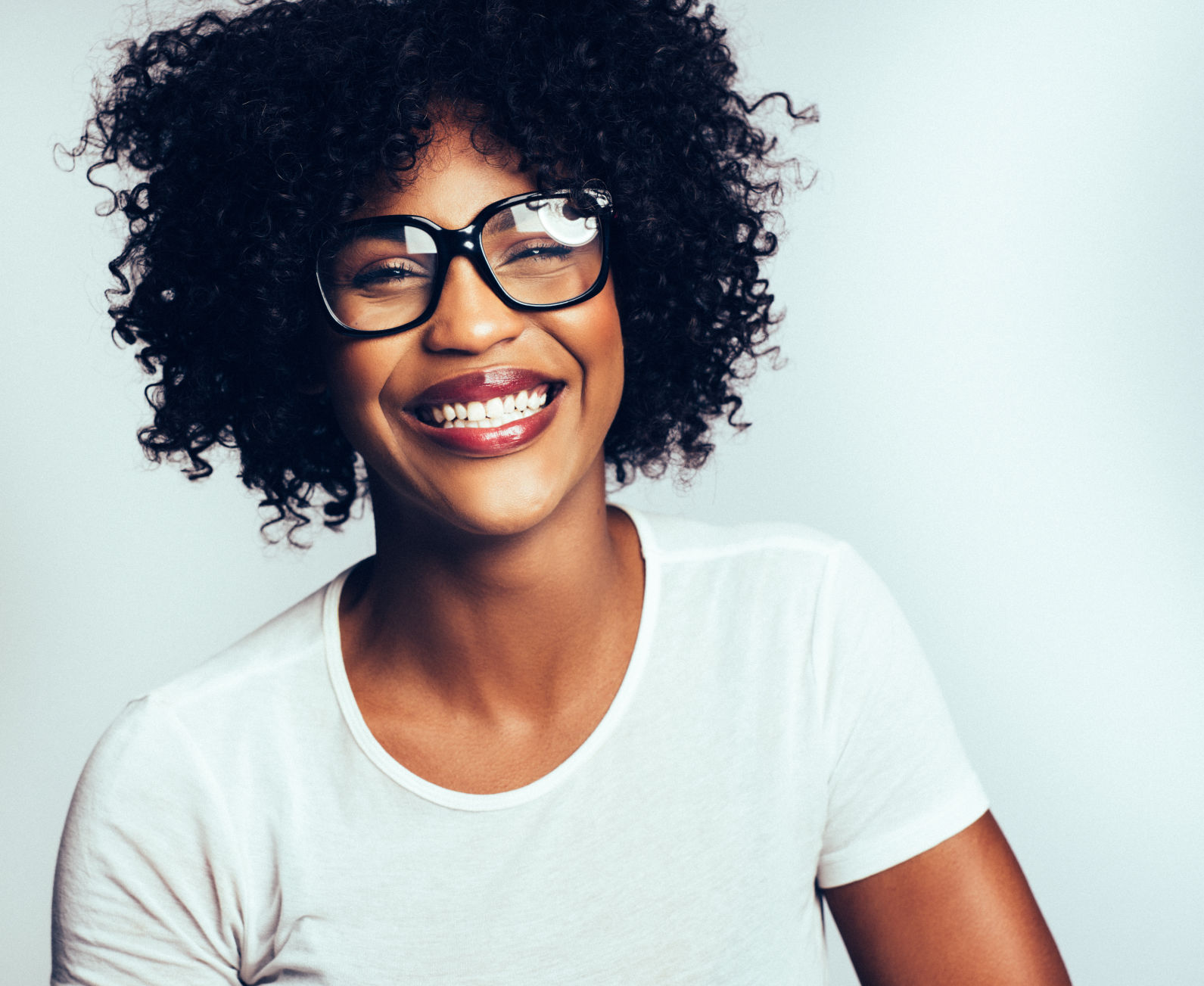 Young African woman wearing glasses laughing against a gray background